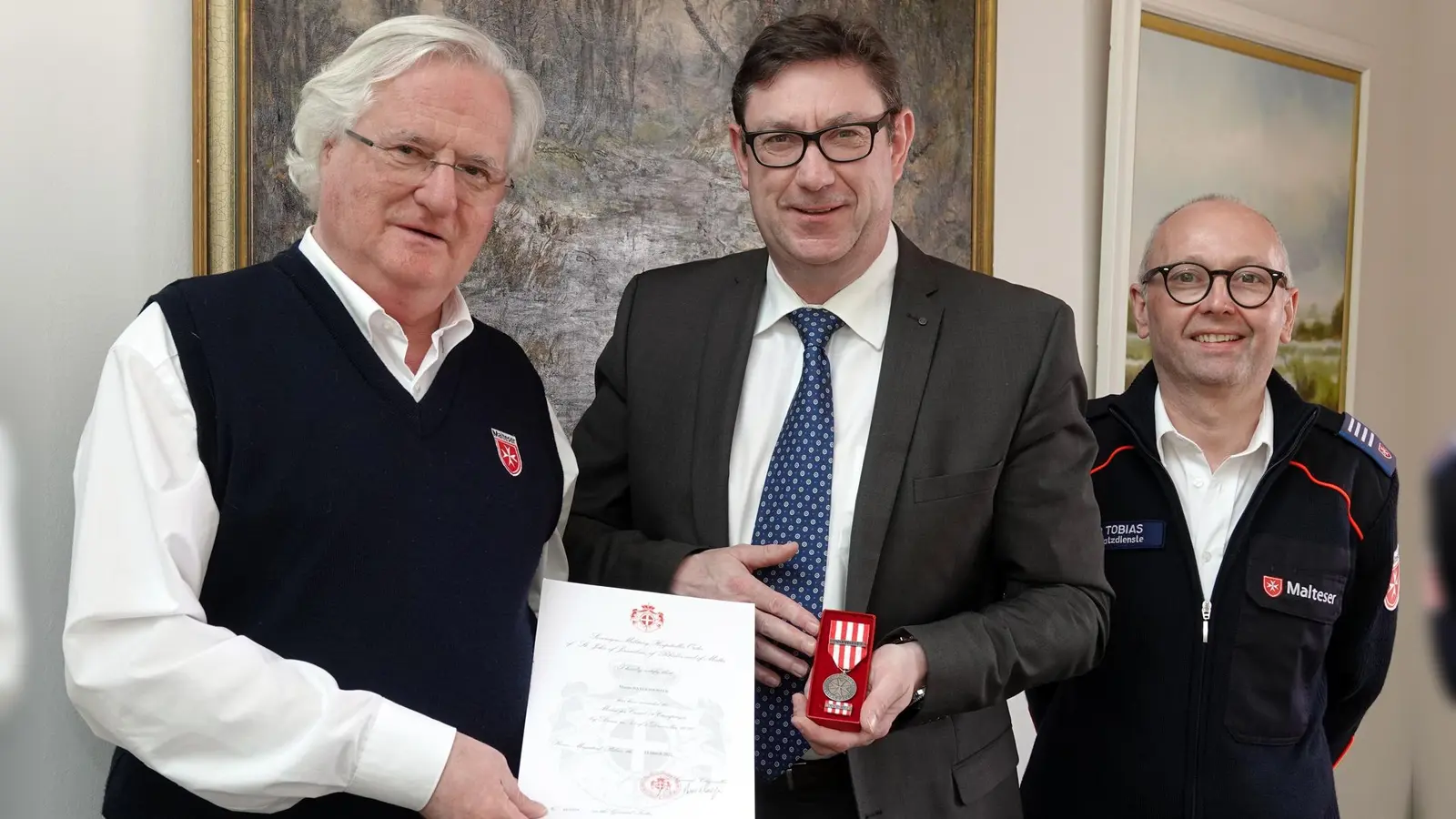 Franz Xaver Graf Basselet von La Rosée, Kreisbeauftragter der Malteser Erding, und Tobias Cako, Leiter Einsatzdienste bei der Übergabe der Medaille an Landrat Martin Bayerstorfer (Foto: LRA)